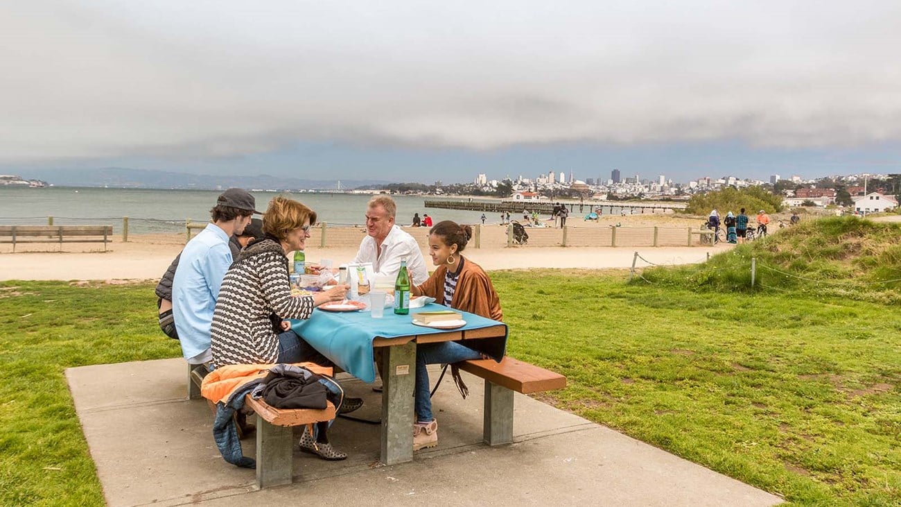 Golden Gate Bridge view from Crissy Field with dogs playing on sandy beaches and open fields.