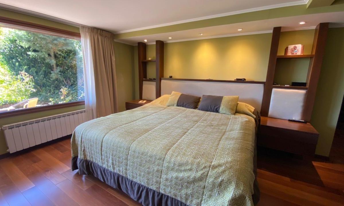 Bedroom with a large patterned bed, dark wood shelving, and a wide window overlooking greenery.