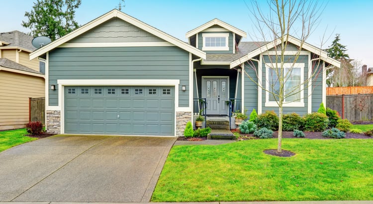 Gray-blue house with a two-car garage, covered entry, and landscaped front yard.