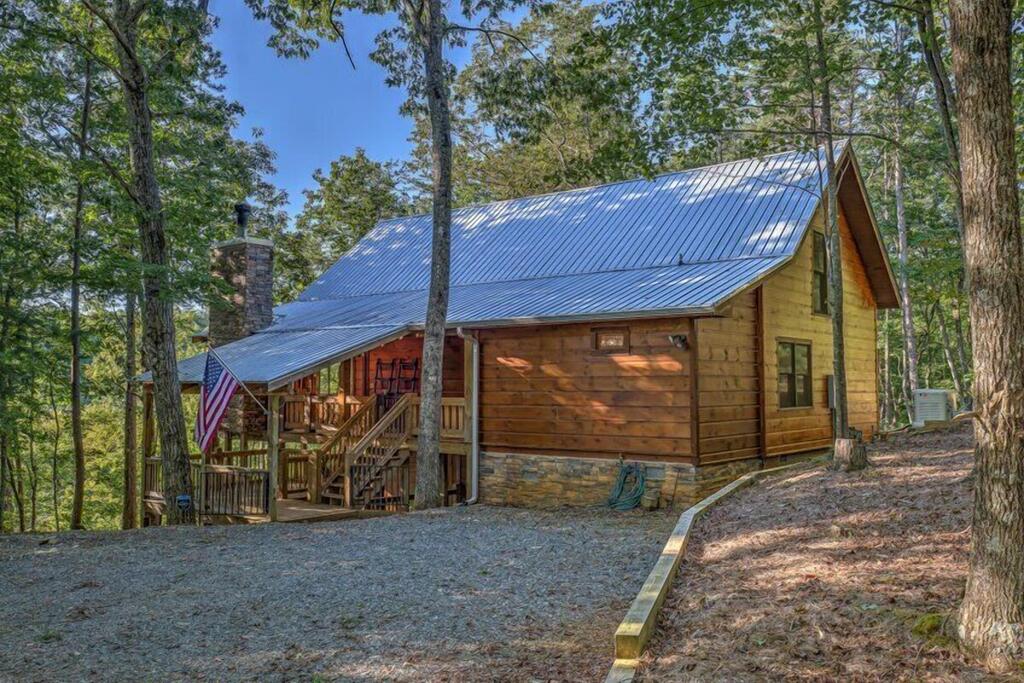 Wooden mountain cabin among trees, with a metal roof, covered porch, and American flag.