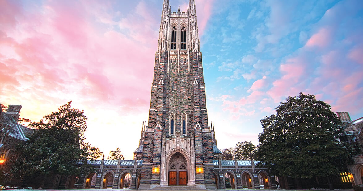 Duke University Chapel’s tall Gothic tower rises beneath a pink-and-blue sunset sky.