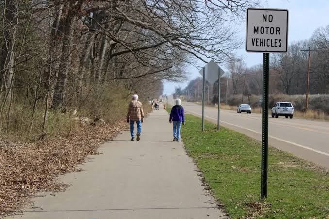 Paved walking path beside a road, with two walkers and a No Motor Vehicles sign.