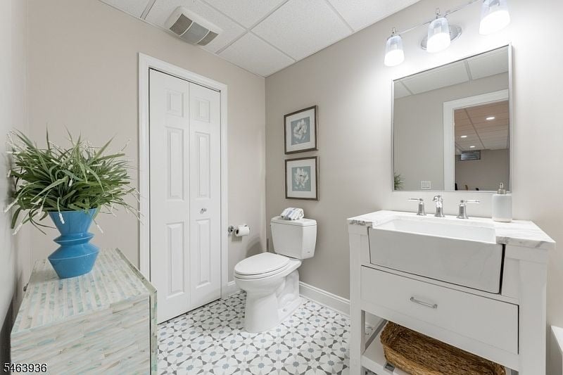Bathroom with a white vanity and large mirror, toilet, and patterned geometric tile floor.