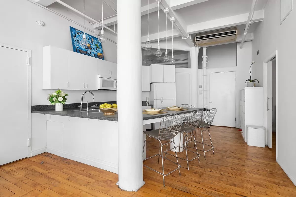 Kitchen and dining area with white cabinets, a breakfast bar, wire stools, and hardwood floors.