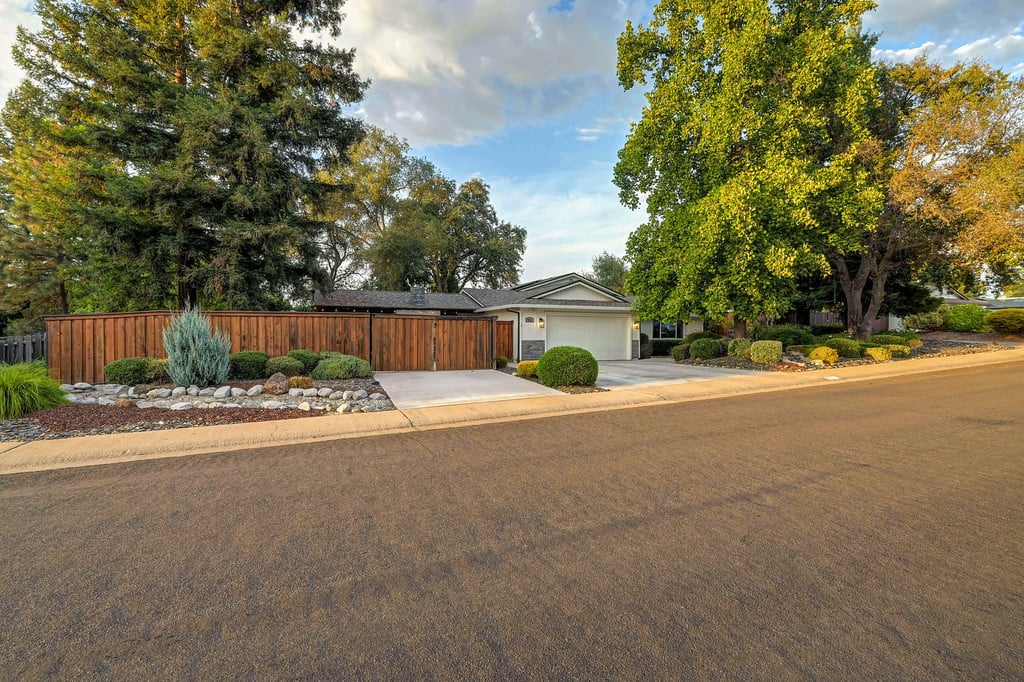 Single-story home with an attached garage, wooden privacy fence, and mature trees along the street.