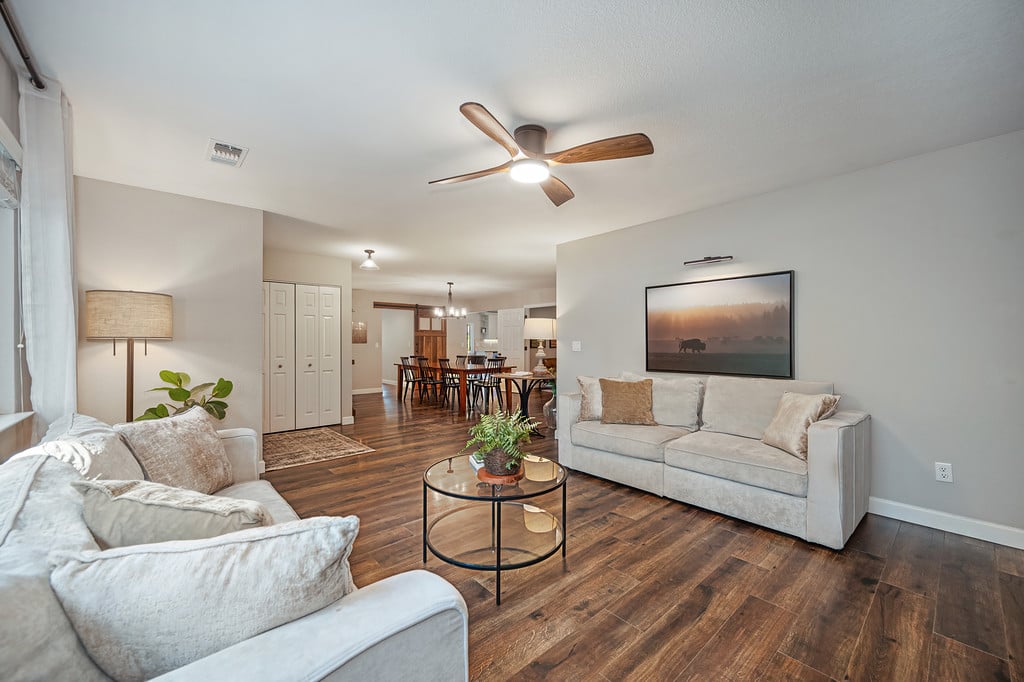 Living room with light sofas and wood floors opening to a dining area.