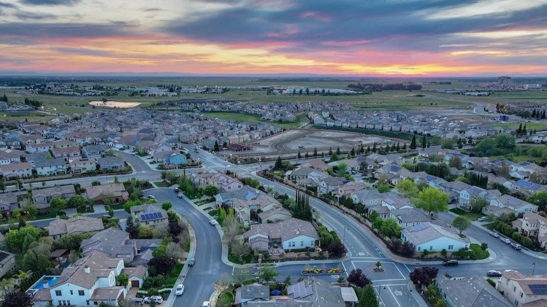 Aerial view of a suburban neighborhood at sunset, with curved streets and detached homes.