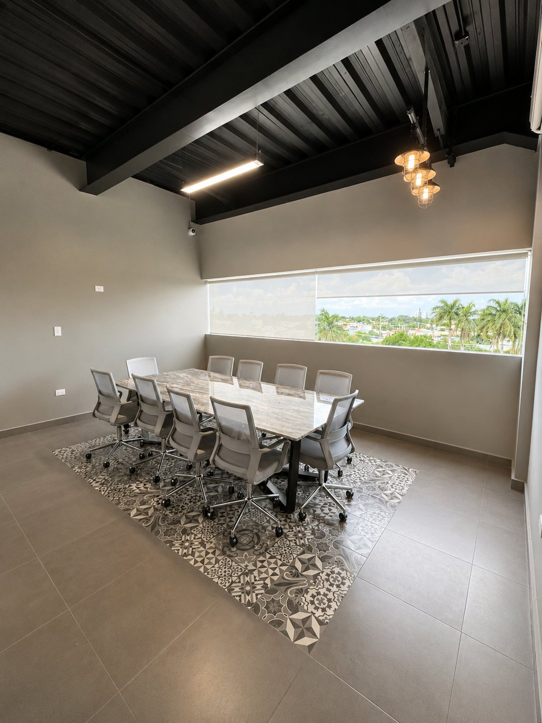 Office conference room with a marble-pattern table, patterned tile rug, and a wide window overlooking palm trees.