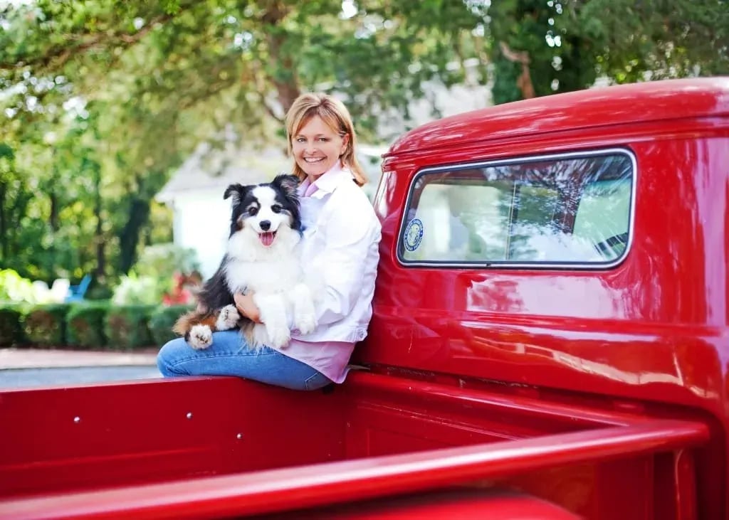 Jamie McDevitt with a dog in a red pickup, exuding casual elegance at a luxury property.