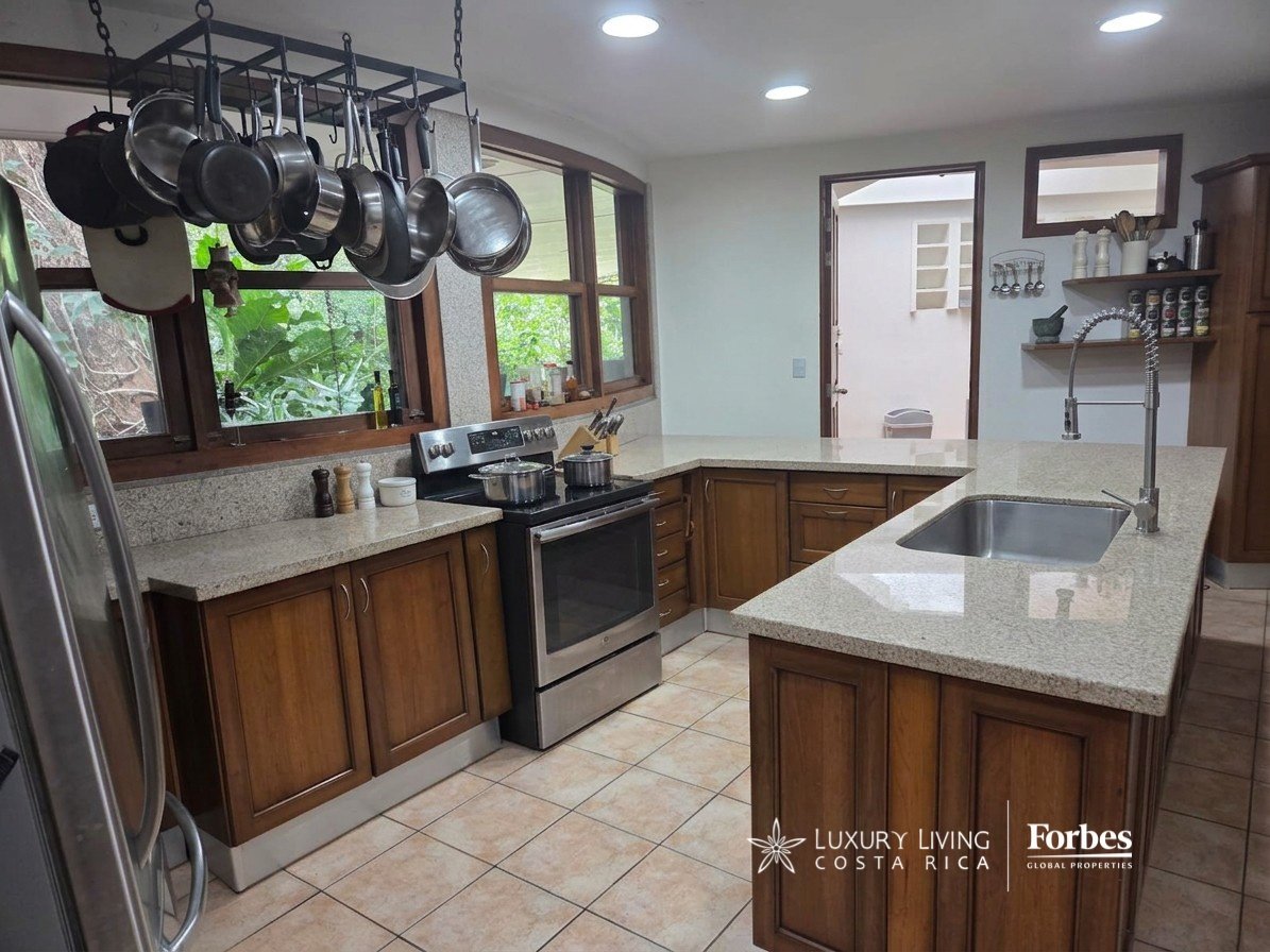 Villa kitchen with a granite island, dark wood cabinetry, stainless steel appliances, and windows overlooking greenery.