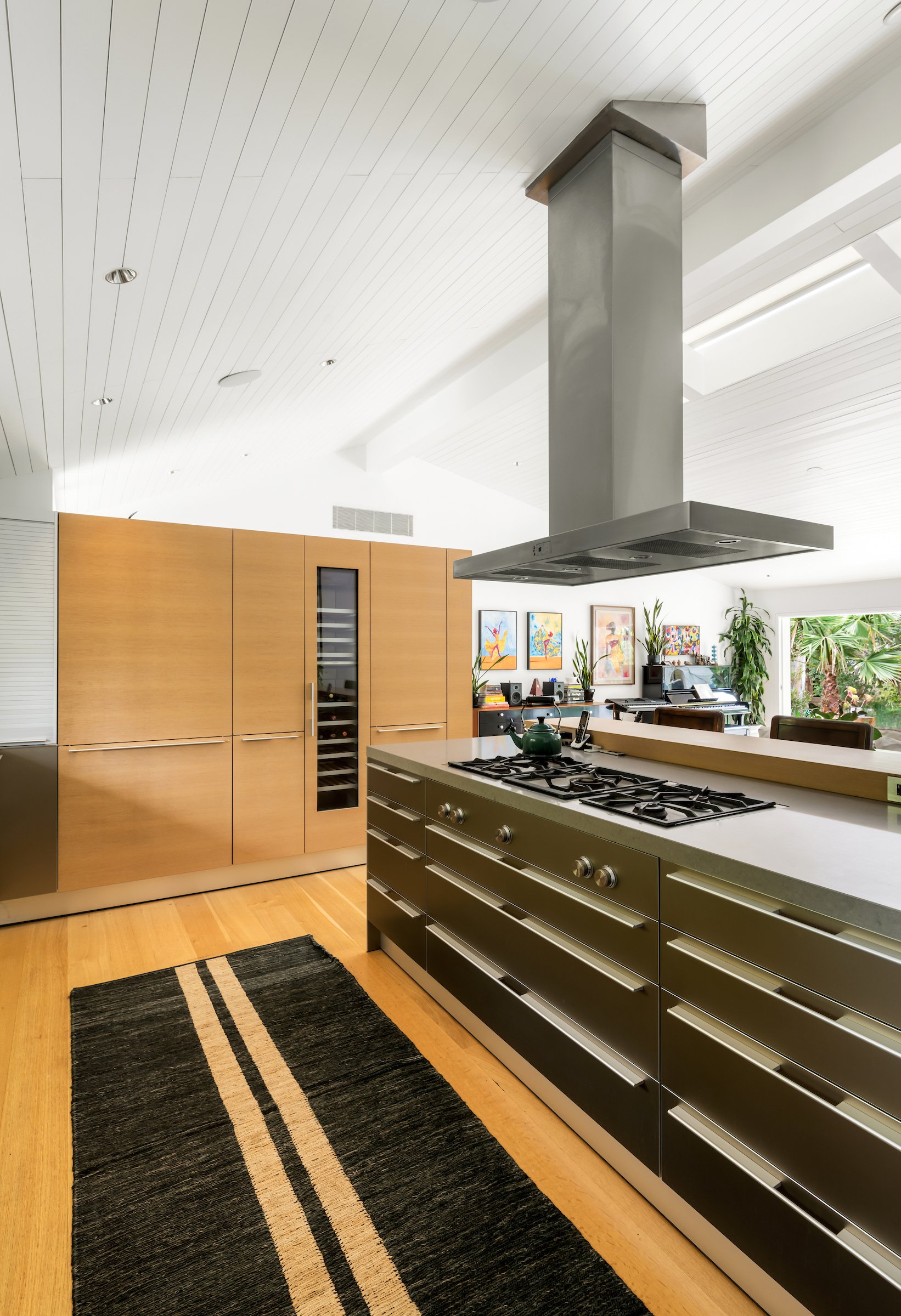 Modern kitchen with wood cabinetry, a multi-burner island cooktop, and a prominent stainless steel range hood.