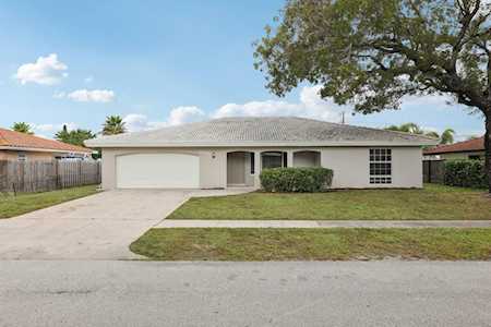 Single-story beige home with a tiled roof, two-car garage, driveway, and large tree at the curb.