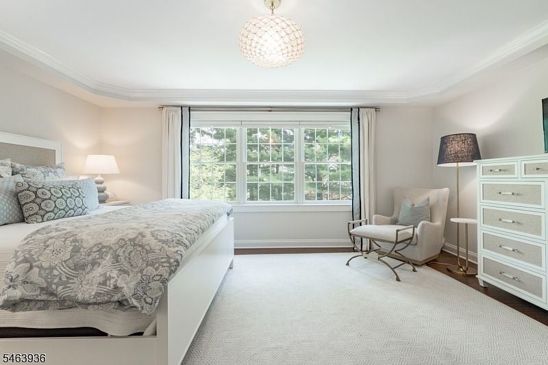 Bright bedroom with gray floral bedding, a large curtained window, and a cozy armchair.