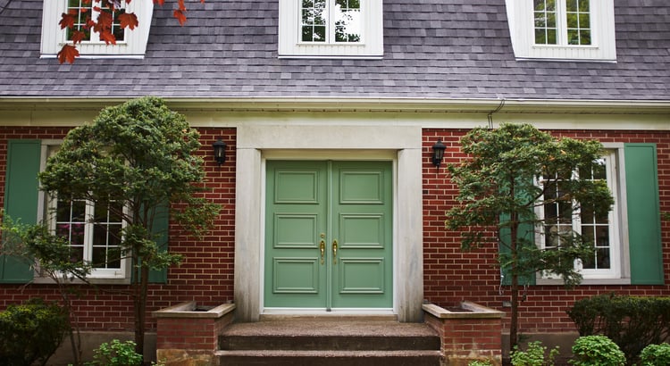 Red-brick house with green double doors, matching shutters, and landscaped front yard.
