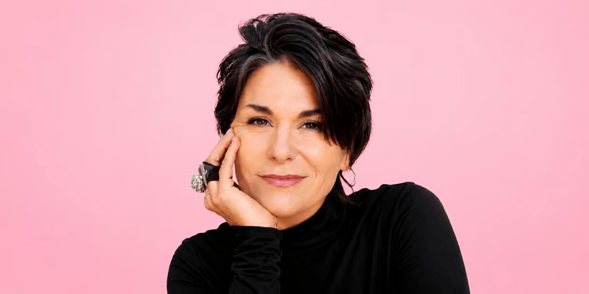 Debbi DiMaggio in a black turtleneck against a pink background.