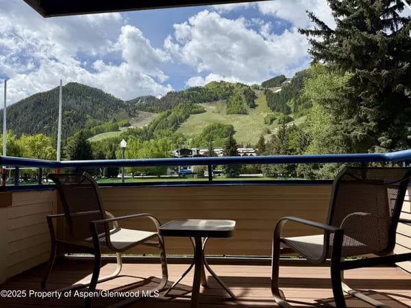 Balcony with two chairs and a table overlooking green mountain slopes and Aspen buildings.