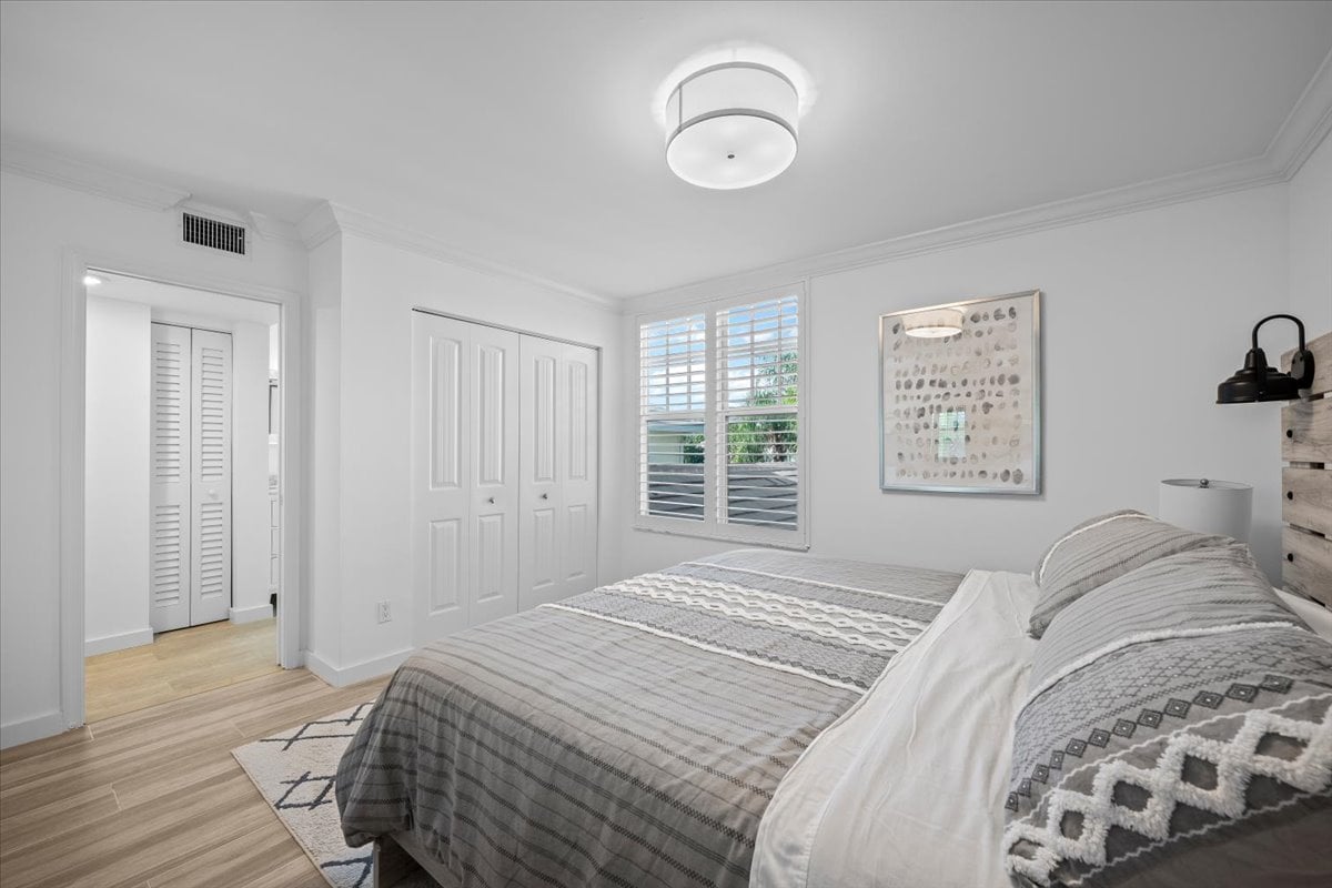 Bedroom with a large gray-patterned bed, plantation shutters, and a double closet.