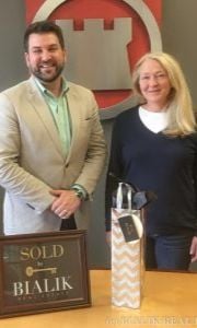 A man and woman pose beside a SOLD sign at a closing celebration.