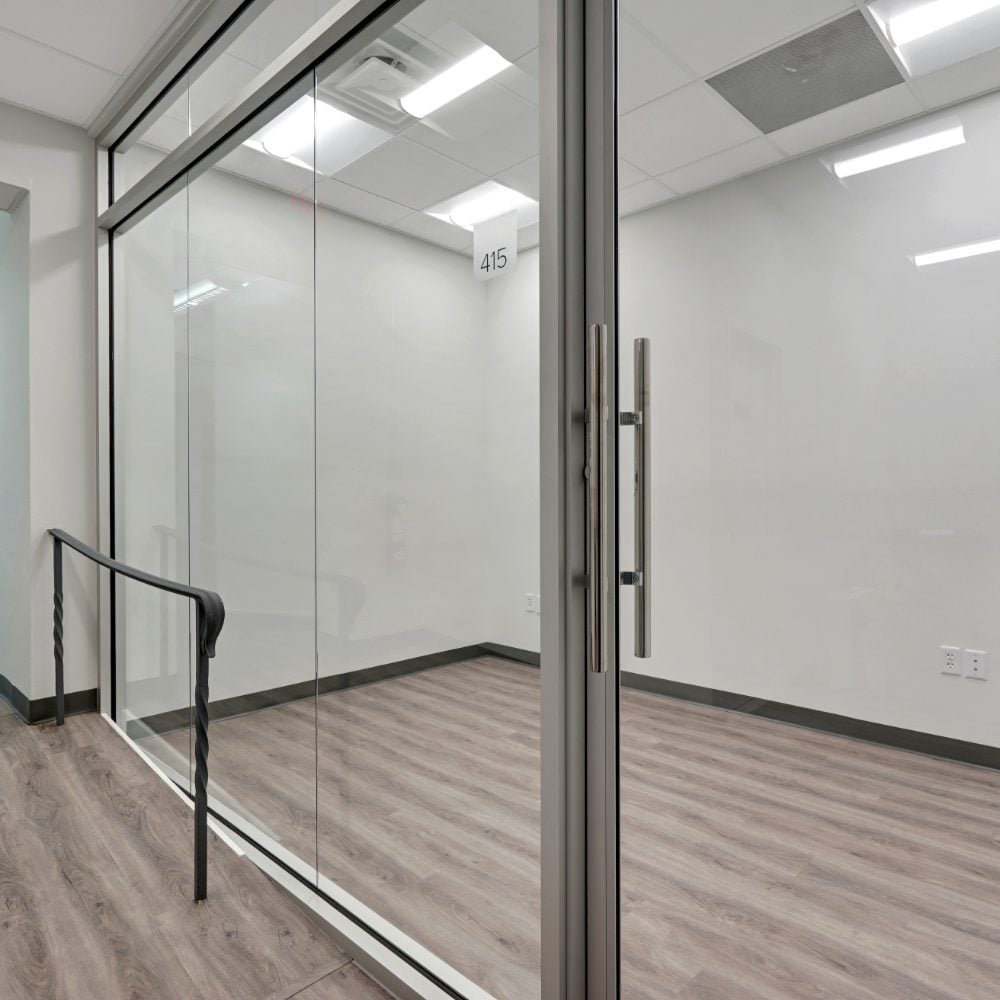 Vacant office with glass walls, gray wood-look flooring, and a door marked 415.