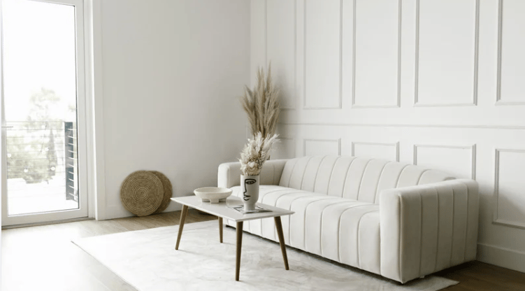 Bright living room with a white channel-tufted sofa, paneled walls, and a low wooden coffee table.