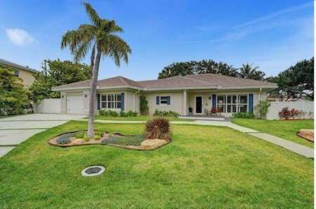 Single-story home with a broad lawn, palm tree, landscaped garden bed, and garage.