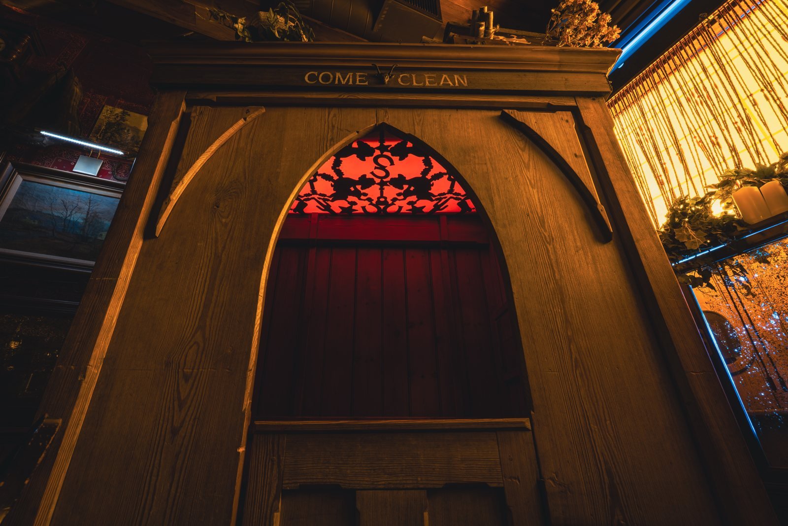 A carved wooden confessional booth with a red-lit arched window at Cowboys and Poodles.