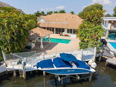 Waterfront home with a pool and dock, seen above a canal with a blue-and-white boat.
