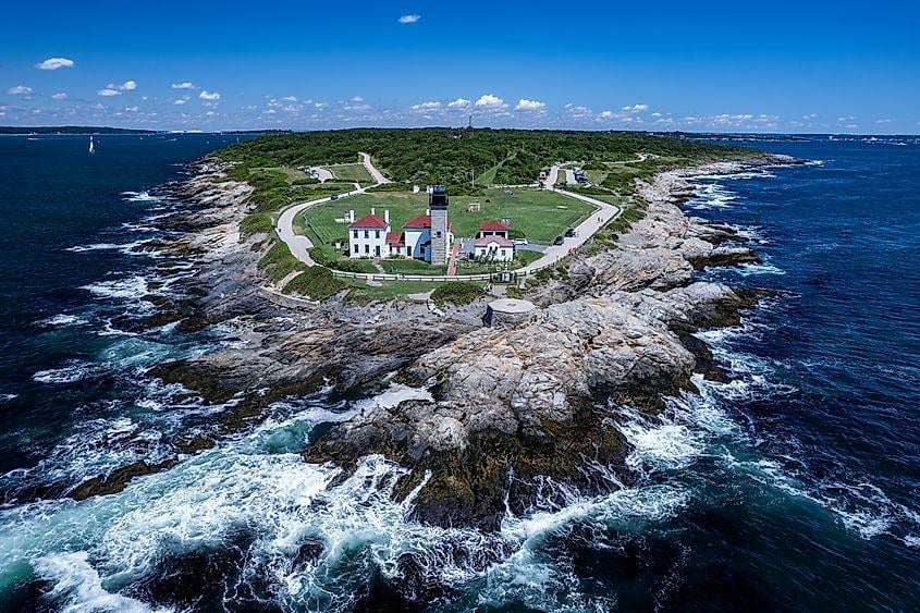Beavertail Lighthouse on a rocky point, surrounded by ocean and breaking waves.