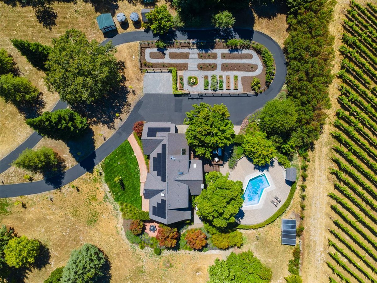 Aerial view of a home with a swimming pool, landscaped gardens, and vineyard rows.