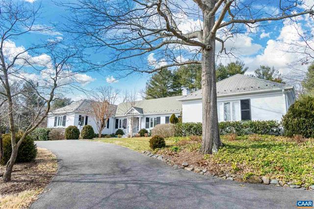 White single-story house beside a paved driveway, framed by a large leafless tree.