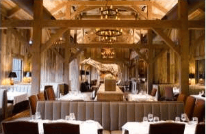 Restaurant dining room with white-clothed tables beneath exposed timber beams.