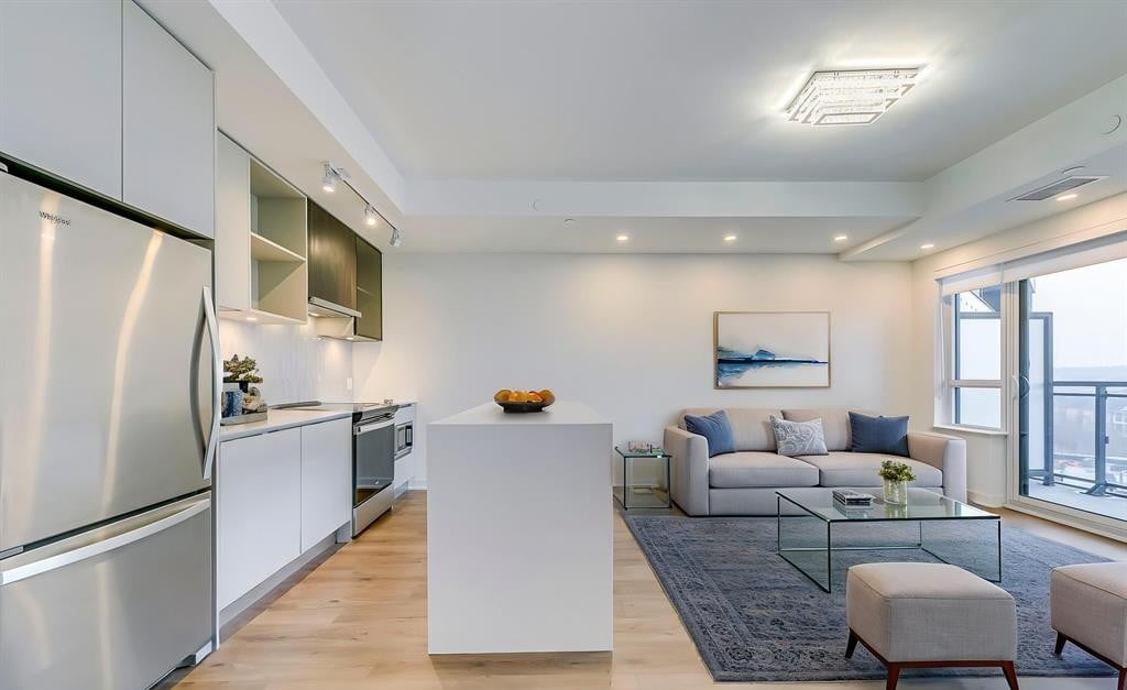 Open-concept condo kitchen and living room with a white island, gray sofa, and balcony doors.