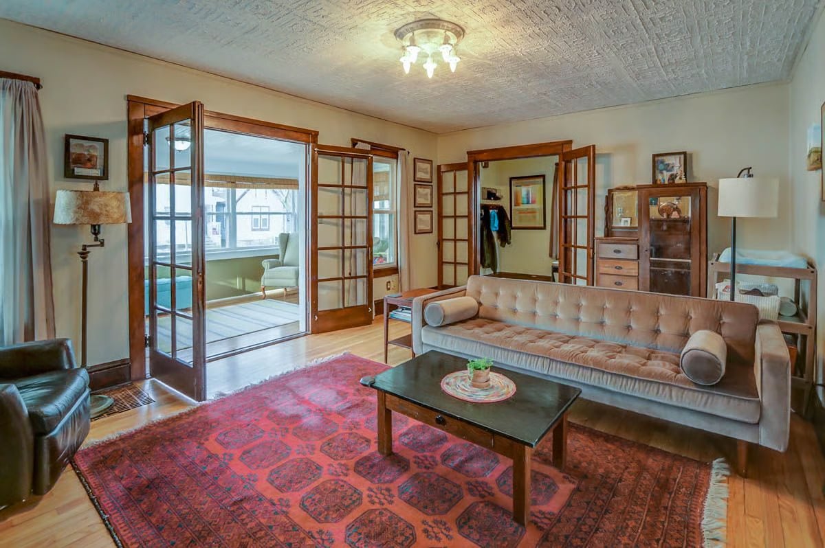 Living room with a tufted sofa, patterned rugs, and open French doors to a bright sunroom.