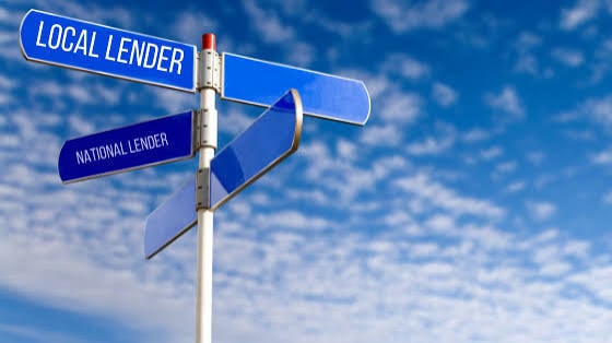 Sign pointing to local lender and national lender against a blue sky.