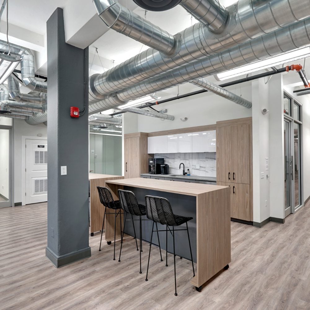Kitchen and break area with a wood-paneled island, black stools, and exposed ventilation ducts.