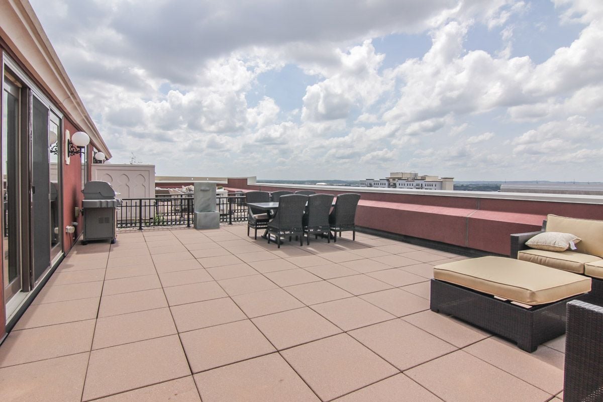 Rooftop terrace with tiled paving, outdoor dining set, cushioned lounge chairs, and distant buildings.