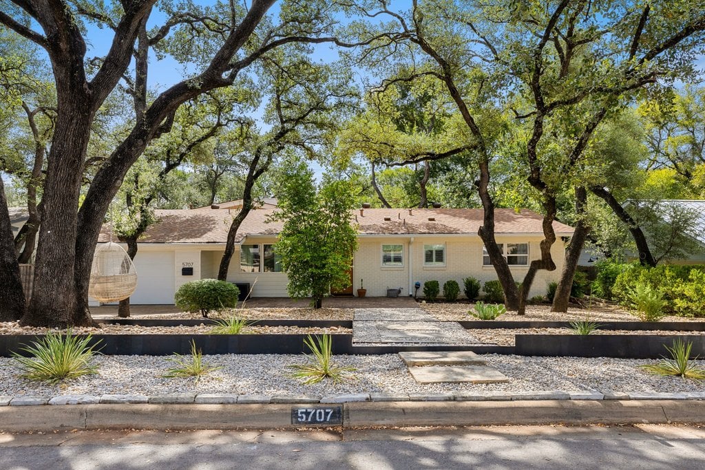 Single-story home framed by mature oak trees, with a gravel front yard and curb address 5707.