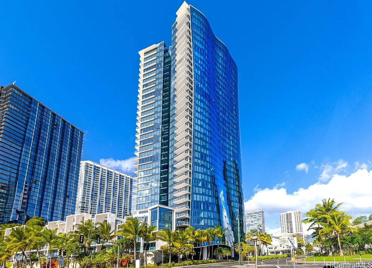 High-rise condominium with a curved blue-glass facade and balconies, framed by palm trees.