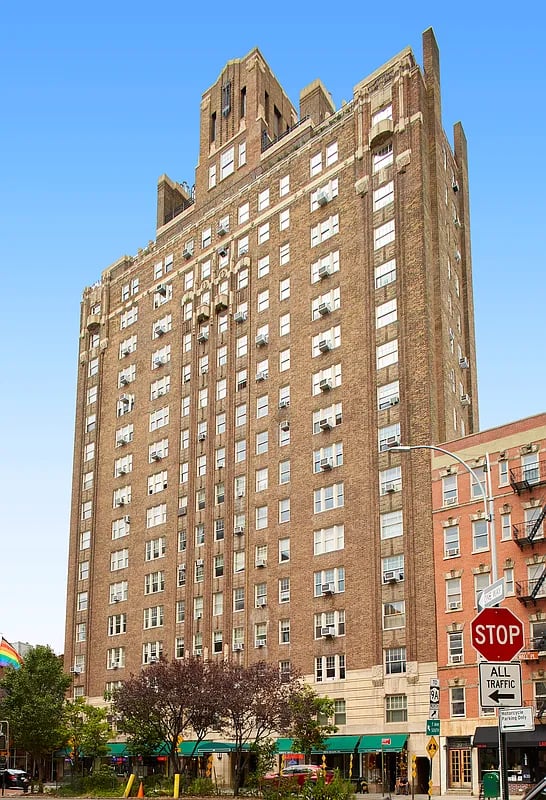 Tall brown brick apartment building with stepped upper stories and rows of windows above street-level storefronts.