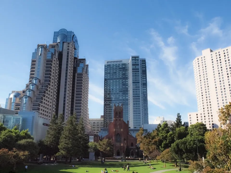 The green lawns of Yerba Buena Gardens with a red brick church and modern skyscrapers in the background.