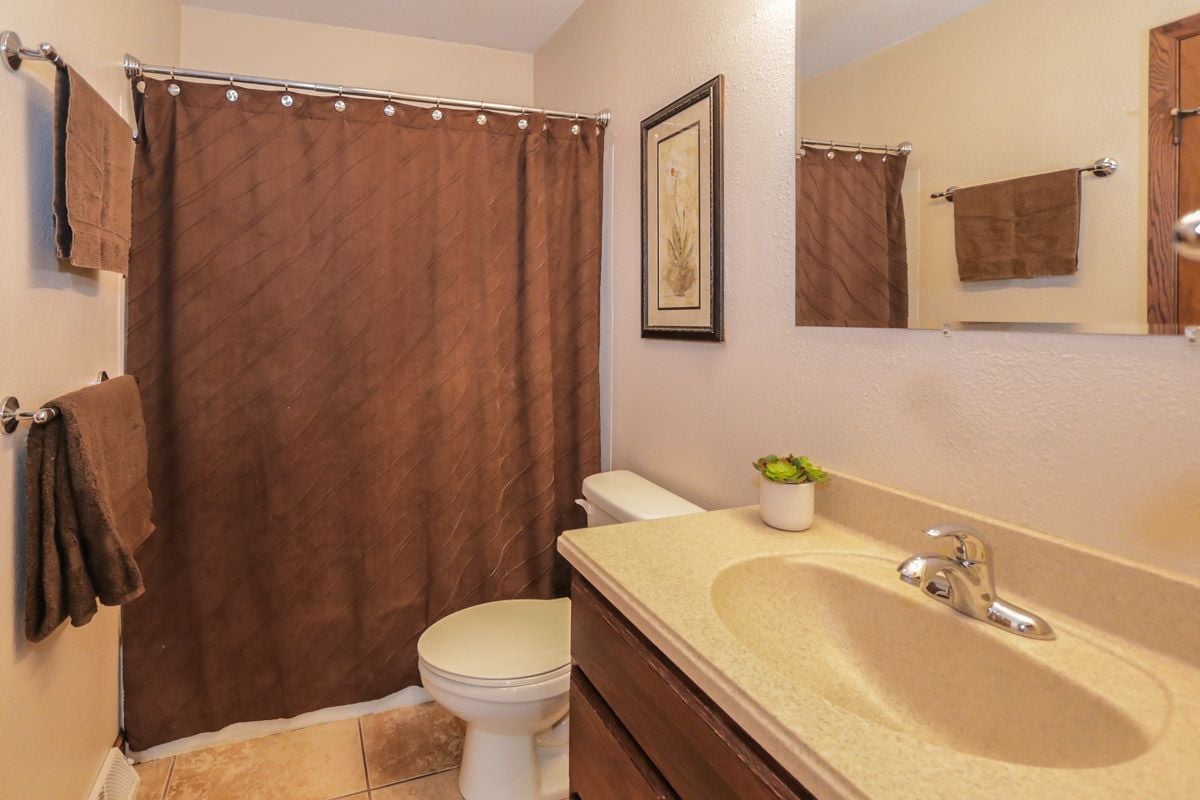 Bathroom with brown shower curtain and towels, toilet, and beige vanity with oval sink.