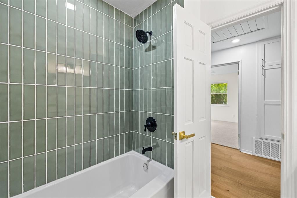 Bathroom with sage-green tile around a white bathtub and black shower fixtures, viewed through an open doorway.