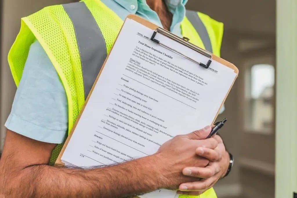 Person in a safety vest holding a clipboard with a home inspection checklist.