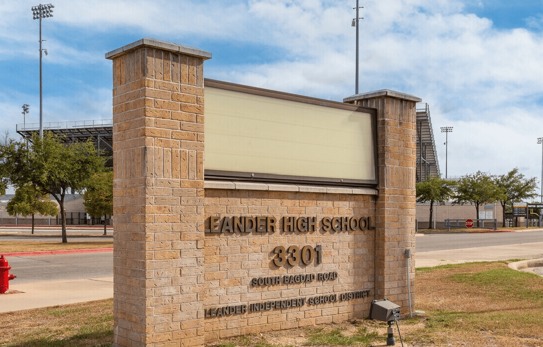 Leander High School entrance sign with stadium bleachers and lights in the background.