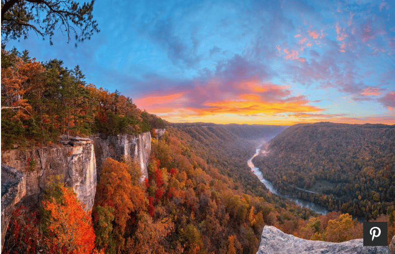 Autumn river valley from a rocky overlook, with forested cliffs beneath a vivid sunset.