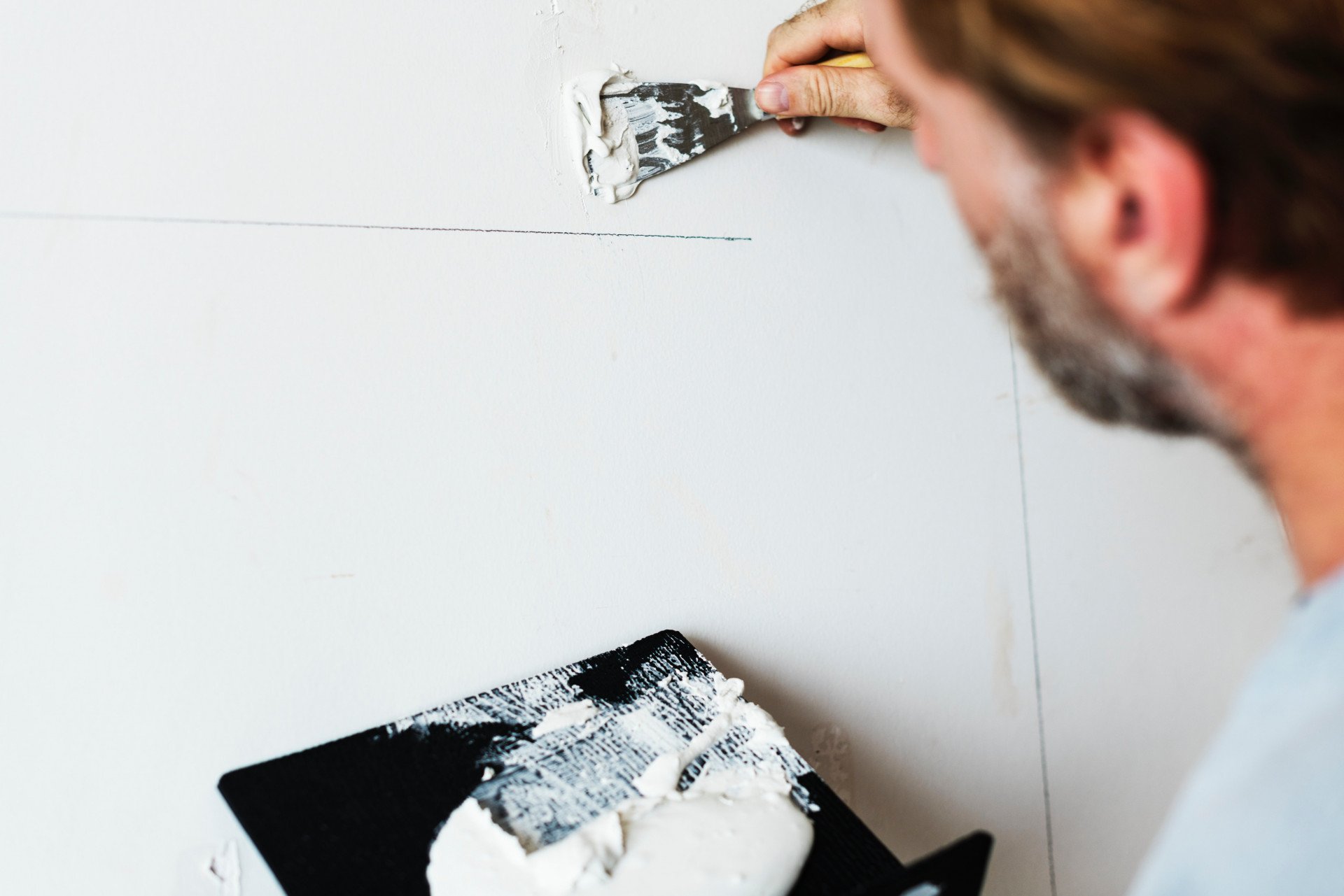 A man spreads joint compound over a seam in a wall with a putty knife.