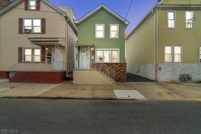 Sage-green two-story house with brick facade and front steps, between two neighboring homes.
