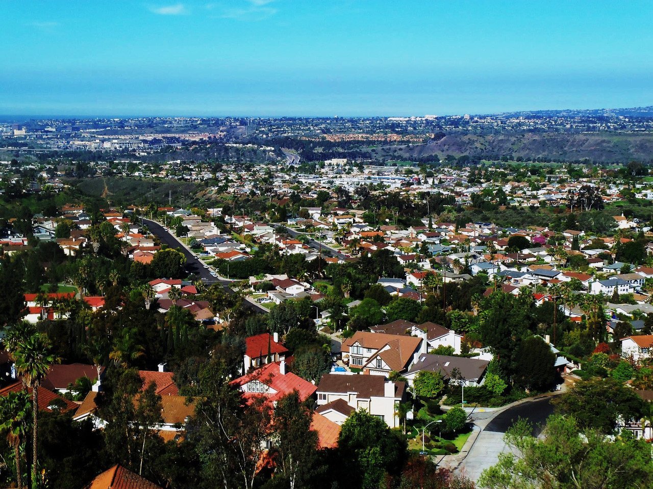 Aerial view of Del Cerro neighborhood in San Diego showing hillside homes, tree-lined streets, and sweeping views toward Mission Valley—ideal for buyers seeking space, views, and value.
