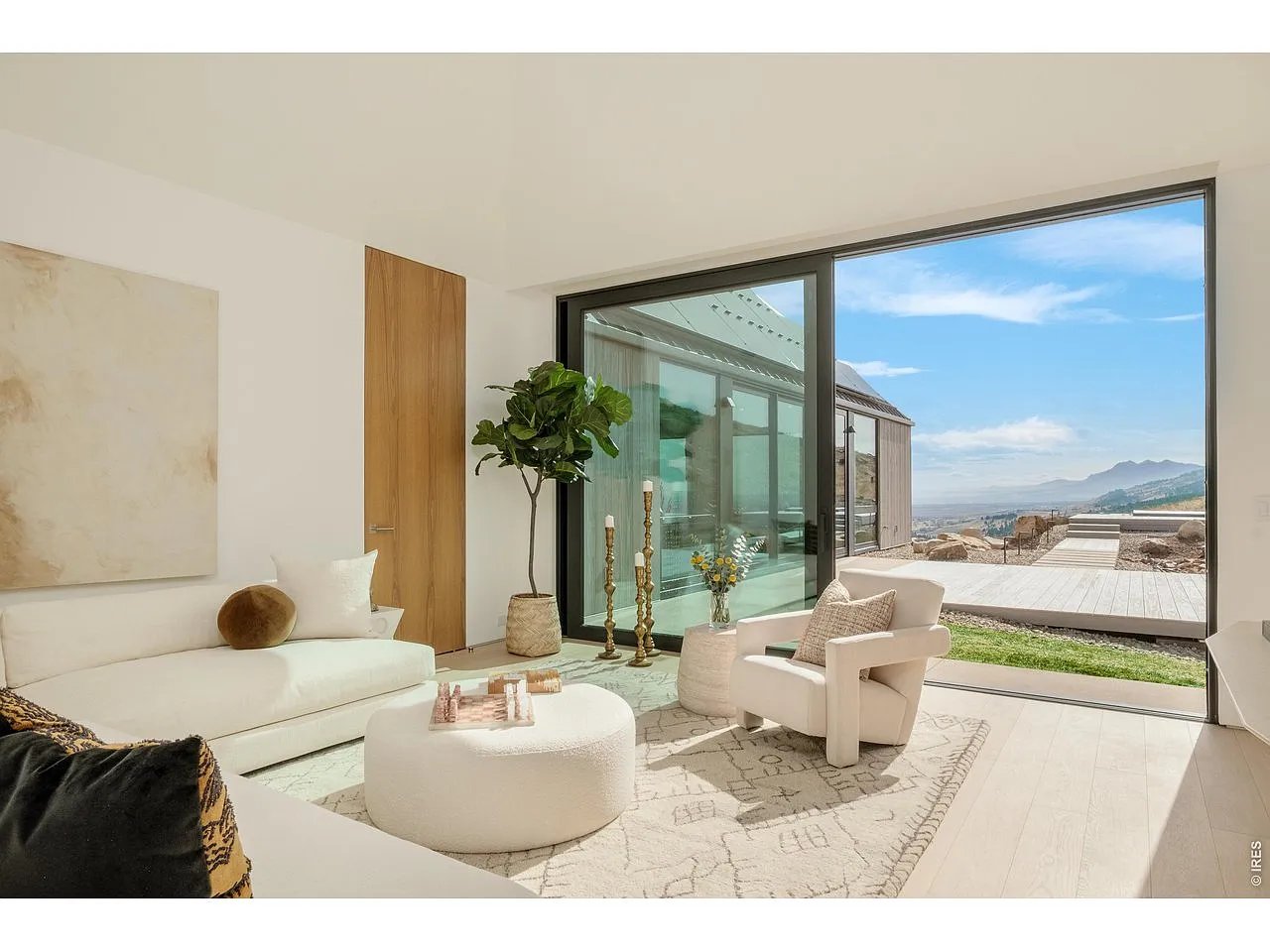 Bright living room with white furnishings and floor-to-ceiling windows overlooking mountains.