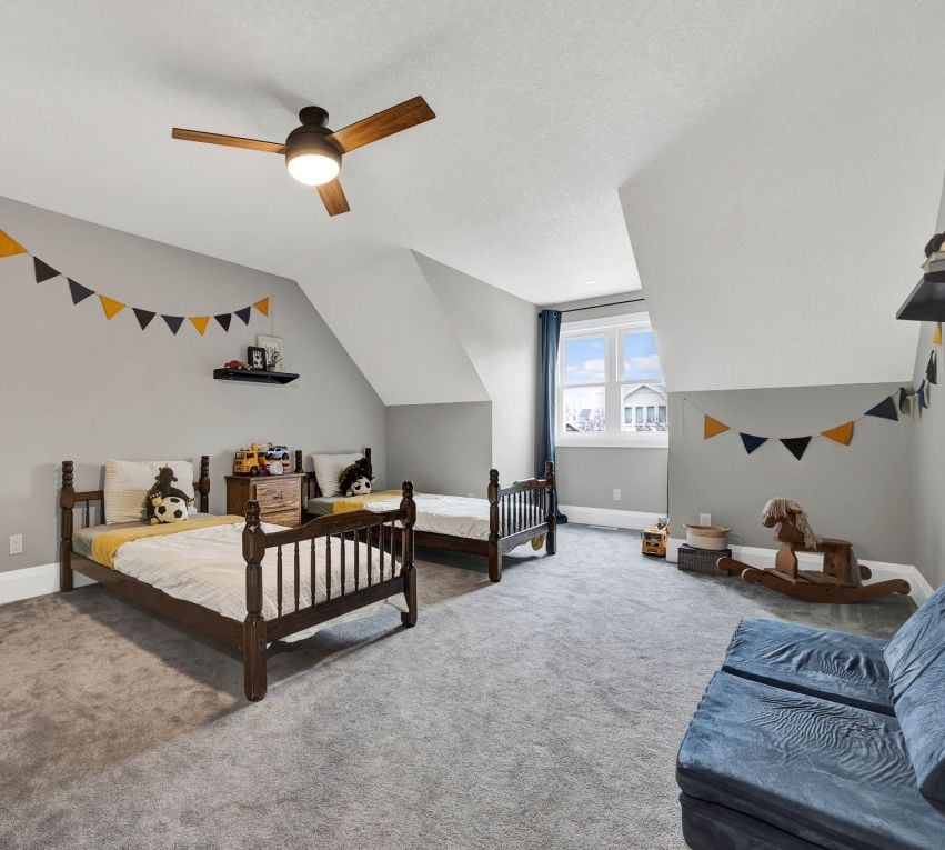 Attic bedroom with two wood twin beds, gray carpet, and colorful bunting.